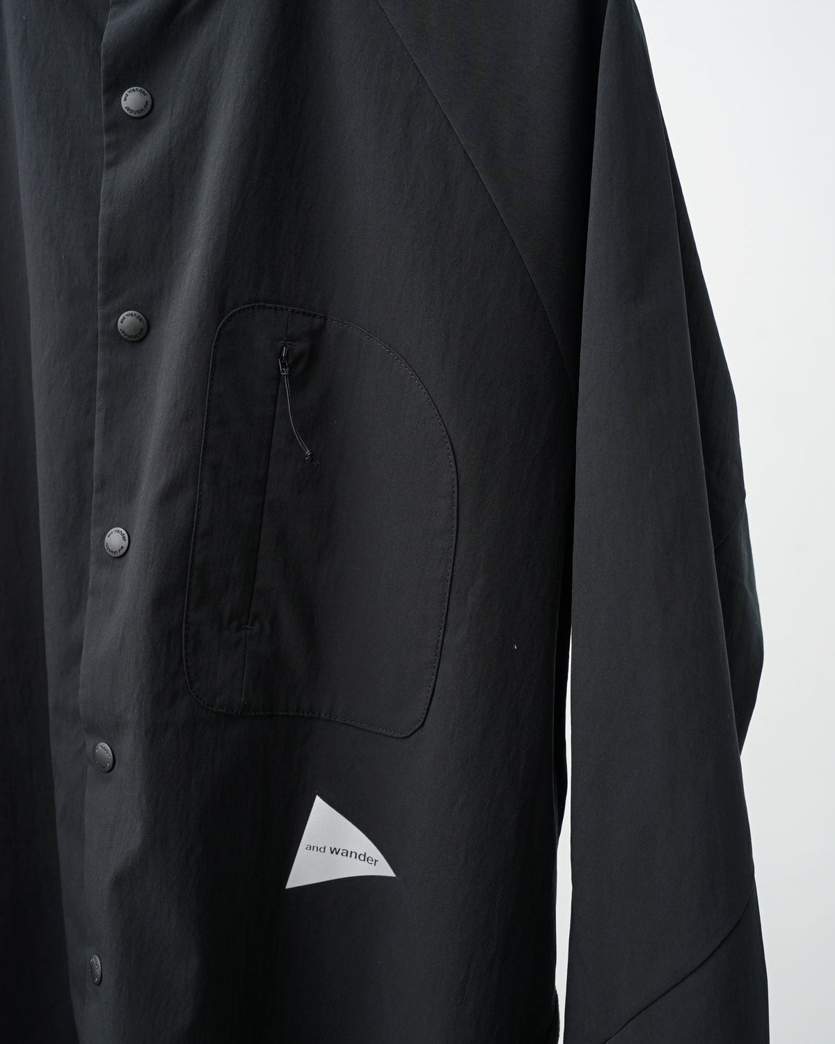 and wandar　fleece base band collar shirt（black）。胸のジップポケットとリフレクターロゴのアップ。